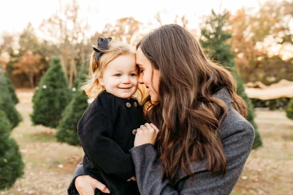 a mother kisses her daughter during their christmas tree farm mini session at Wells Christmas Tree Farm in Norman, OK
