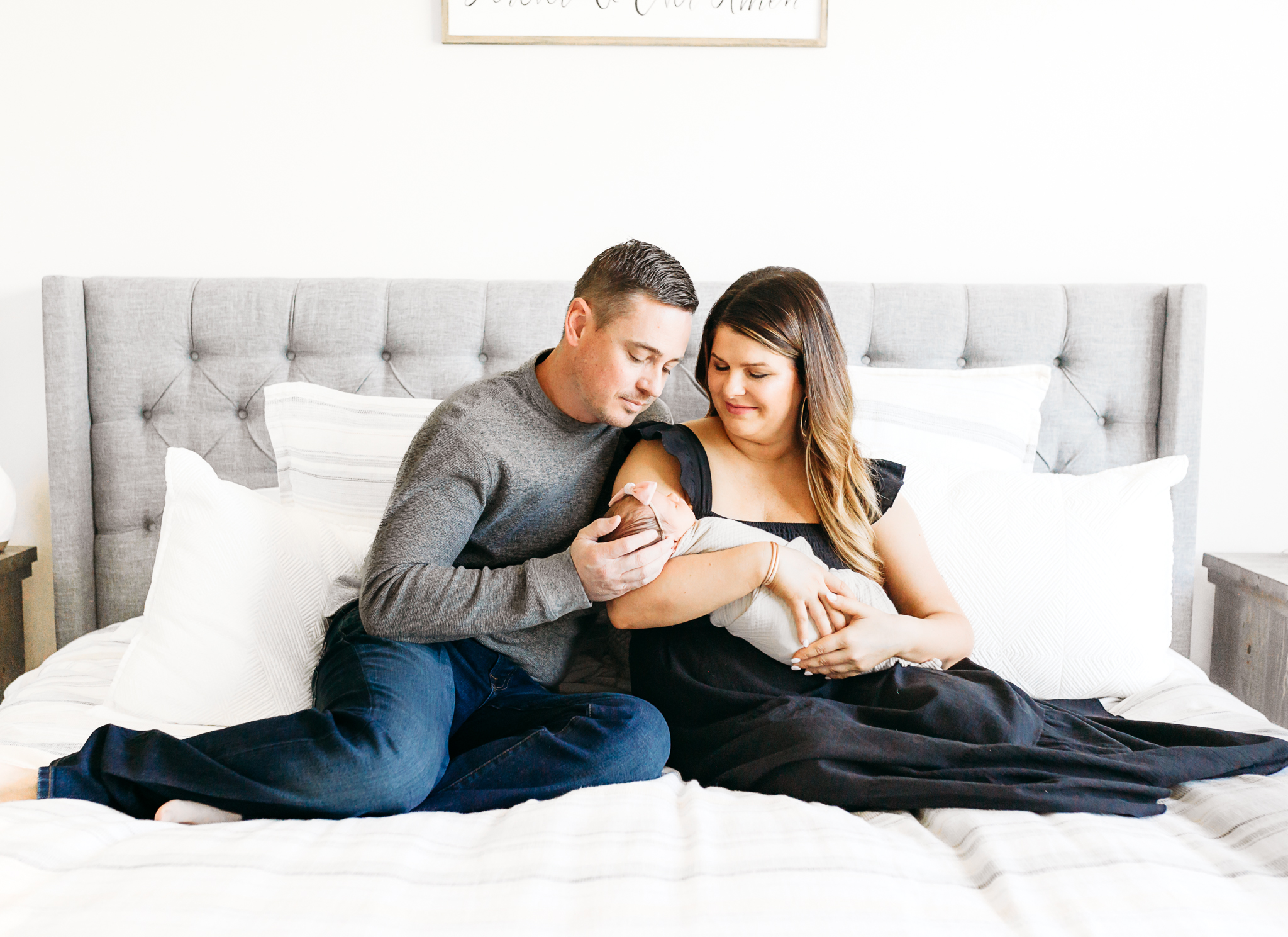 A mom and dad sit with newborn on bed.