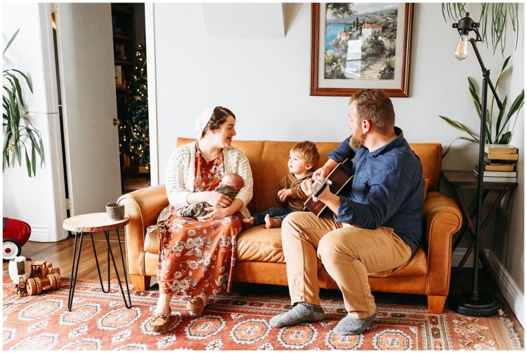 Family of four sits in living room during newborn photo session.