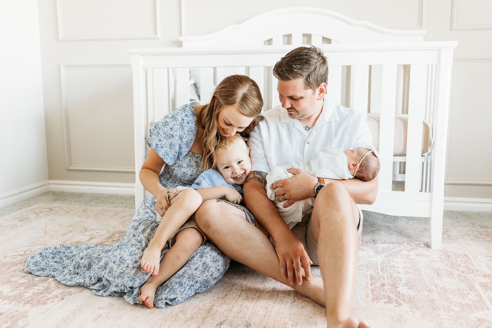 Family of 4 sits in newborn nursery during photo session with Charis Elisabeth Photography.