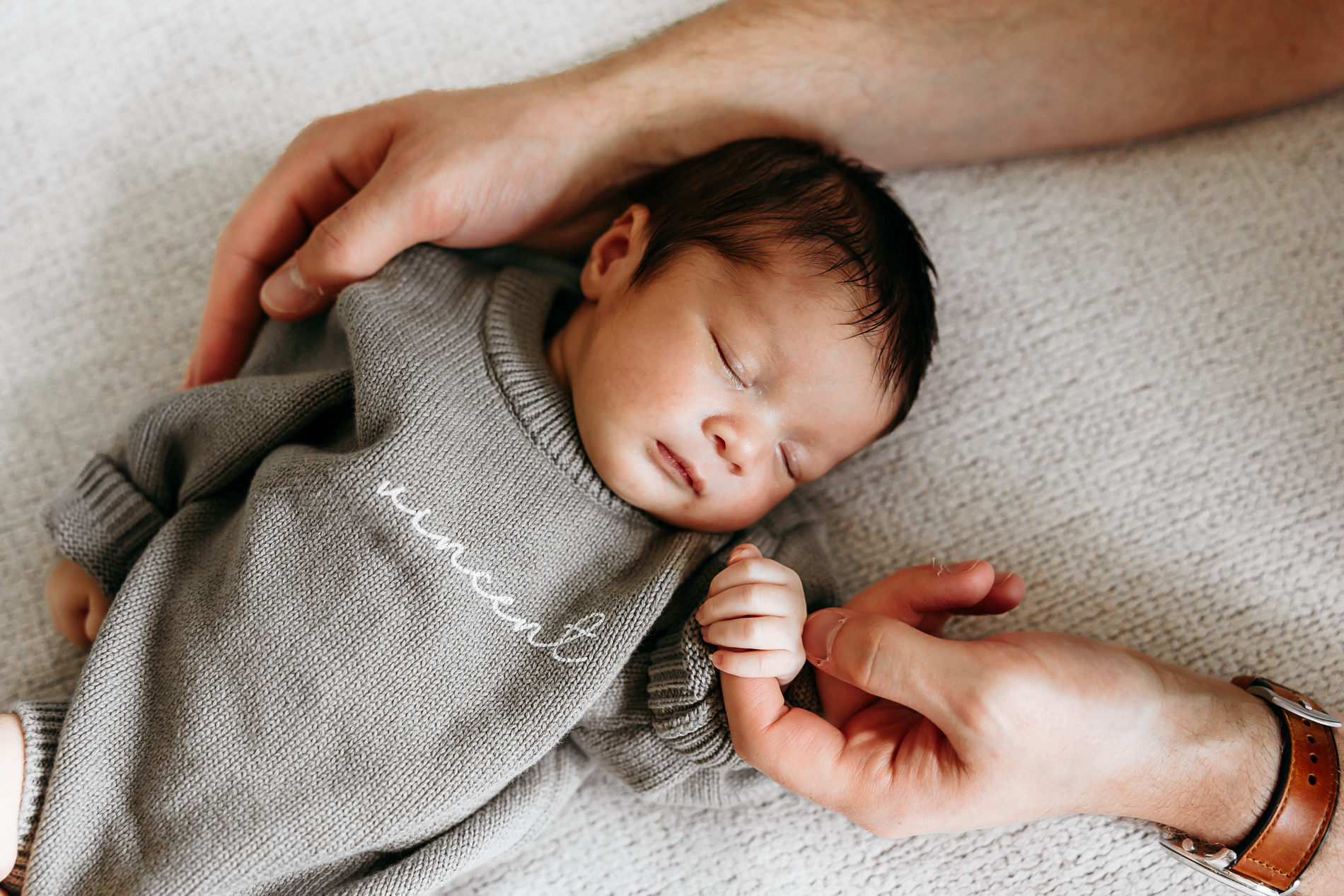 Baby holds dad hand.